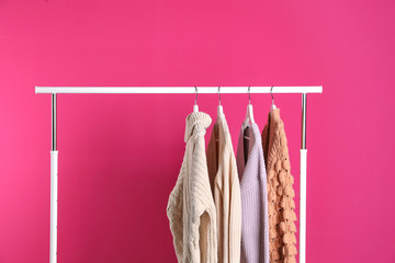Collection of warm sweaters hanging on rack against color background