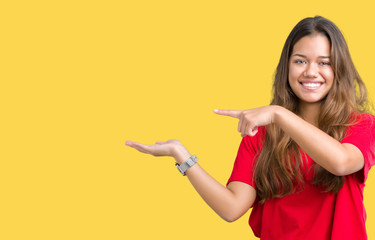Fototapeta na wymiar Young beautiful brunette woman wearing red t-shirt over isolated background amazed and smiling to the camera while presenting with hand and pointing with finger.