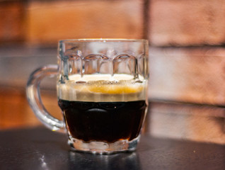 Close up on a glass of dark beer on wooden table in bar on brick wall background