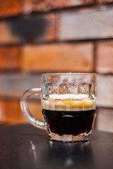 Close up on a glass of dark beer on wooden table in bar on brick wall background