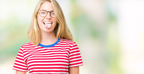 Beautiful young woman wearing glasses over isolated background sticking tongue out happy with funny expression. Emotion concept.