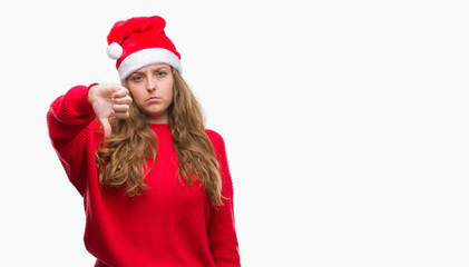 Young blonde woman wearing santa claus hat with angry face, negative sign showing dislike with thumbs down, rejection concept