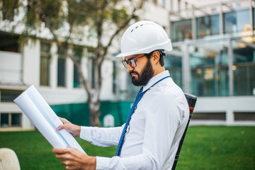 Young architect at work with helmet and plans for the project in hand