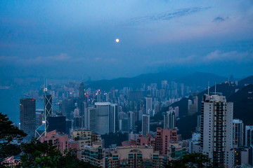 Full moon rise over Hong Kong Skyline at dusk, sunset. Modern city with with skyscrapers near the sea
