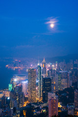 Full moon rise over Hong Kong Skyline at dusk. Modern China city with skyscrapers near the ocean