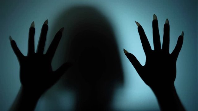 Possessed woman beating on glass, scratching it with sharp nails, witch, ghost. Blood-chilling horror thriller shot