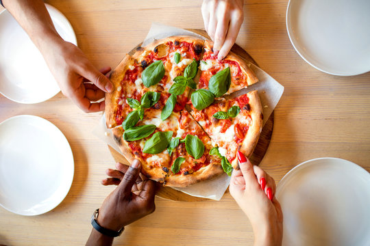 High Angle Shot Of Unrecognizable Mixed Race People's Hands Each Grabbing A Slice Of Pizza