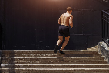 Full length of young African man in sports clothing running down the stairs while exercising...