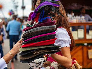 Young lady in tyrolean costume holding a stack of traditional hats, Oktoberfest, Munich, Germany