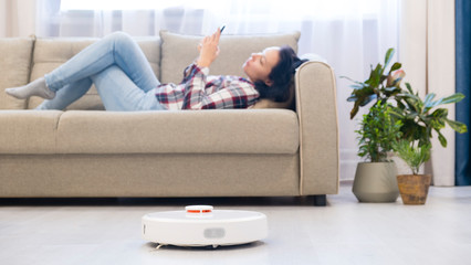 girl resting at home on the couch, while the robot vacuum cleaner. concept time for yourself. smart House. modern girl optimizes her time.