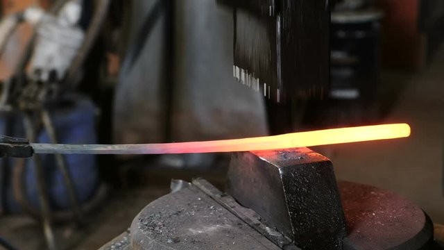 Using pneumatic hammer to shape hot metal. Making the sword out of metal. Side view.