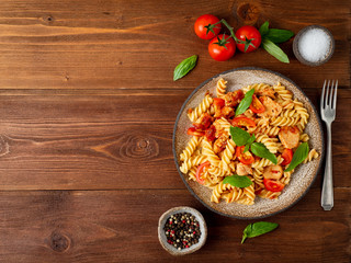 fusilli pasta with tomato sauce, chicken fillet with basil leaves on dark brown wooden background, copy space, top view