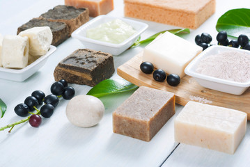 cosmetic clay, soaps, henna blocks, sponge and moisturizer on white wood table