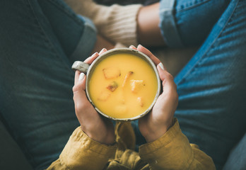 Flat-lay of female in yellow shirt and jeans sitting and keeping mug of Fall warming yellow pumpkin cream soup with croutons, top view. Autumn vegetarian, vegan, healthy comfort food eating concept