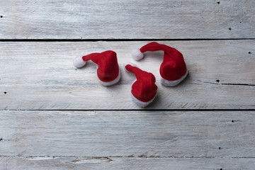 red santa hats on a white, wooden background - greeting card for Christmas