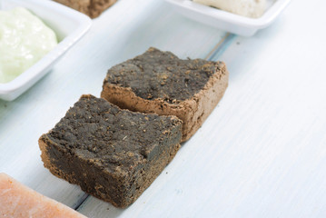 cosmetic clay, soaps, henna blocks, sponge and moisturizer on white wood table