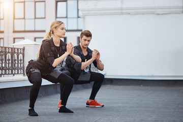 two fit young people bending knees to full squat position. side view full length photo. copy space.