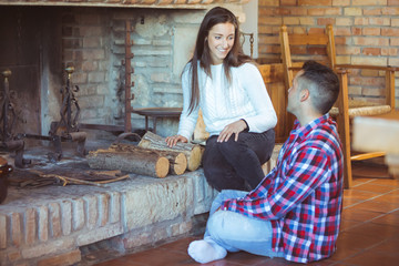 Fototapeta na wymiar Young shy people (man and woman) met at friends party - young couple talking near the fireplace trying to kindle a fire - seduction and love, romantic date, winter holidays celebration concept