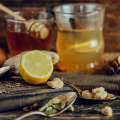 Vitamin healing tea with lemon and honey, ginger and spices on wooden background in rustic style. The concept of spring beriberi and colds. Square image.