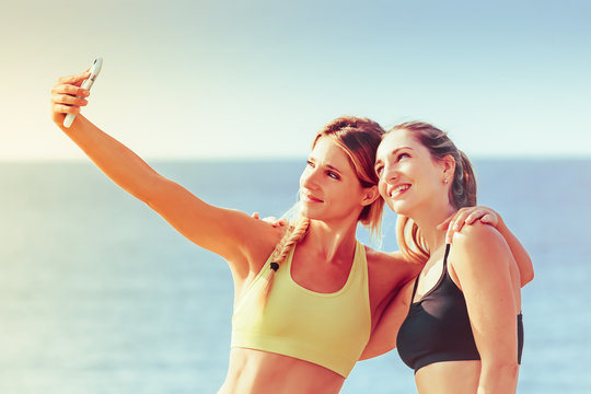 Two young women taking a selfie after a workout: girls taking pictures with a smartphone
