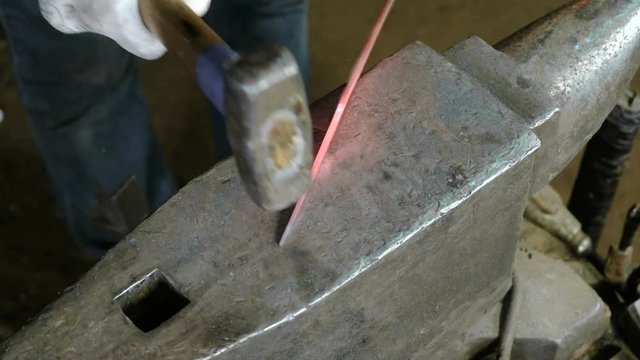 Making the knife out of metal at the forge. Close up blacksmith's hands taking a hammer and hitting hot metal on an anvil. Top view.