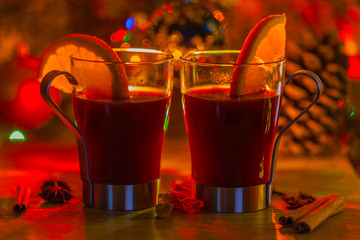 Mulled wine with orange and cinnamon on the red blurred background of Christmas decorations....
