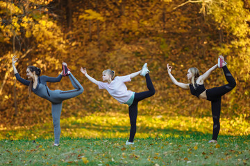 Obraz na płótnie Canvas Group of Young women doing yoga exercises in the autumn city park. Health lifestyle concept.
