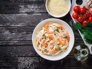 italian pasta spaghetti with shrimps, bechamel sauce and chopped dill on dark rustic wooden table, top view, copy space