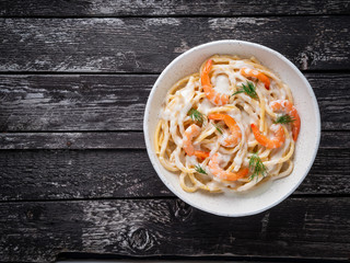 italian pasta spaghetti with shrimps, bechamel sauce and chopped dill on dark rustic wooden table, top view, copy space.