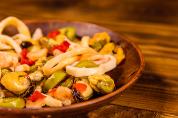 Ceramic plate with different sea food and olives on wooden table