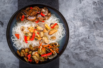 Traditional Asian food - rice noodles with seafood, salad, red pepper and fried mushrooms are on the side table. Copy space. Top view