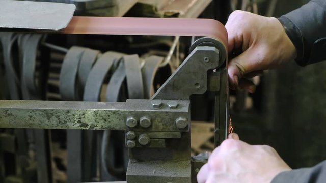 Grinding billets of metal knife on a belt-grinding machine. Close-up of a man's hand.