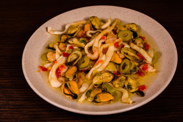 Ceramic plate with different sea food and olives on wooden table