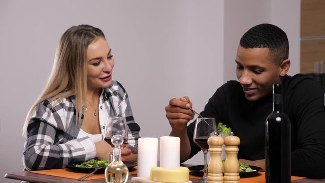 Interracial couple having dinner at candle lights in the kitchen. They drink, eat and smile at each other. Dolly slider 4K footage with parallax effect. Slow motion footage