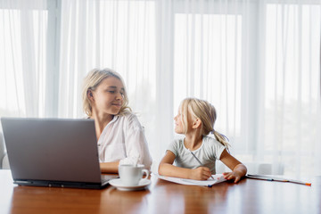 Mother uses laptop at home, child looks at her