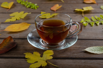 Cup of hot tea on a wooden table with colorful autumn leaves. Fall concept. Selective focus
