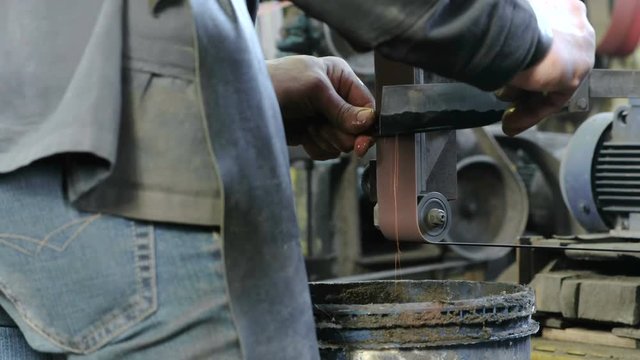 Grinding billets of metal knife on a belt-grinding machine. Close-up of a man's hands.