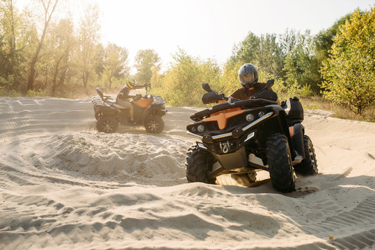 Two atv riders in helmets ride in a circle on sand