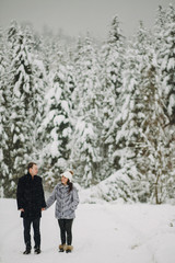 Fototapeta na wymiar Stylish couple in love holding hands and embracing in snowy mountains. Happy family gently hugging and kissing in winter mountains and forest. Holiday getaway together