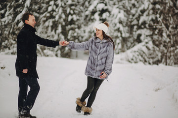 Fototapeta na wymiar Stylish couple in love having fun in snowy mountains. Happy family playing in snow and smiling in winter mountains and forest. Holiday getaway together. Romantic moments