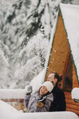 Stylish couple playing with snow in wooden cabin on background of winter snowy  mountains. Happy...