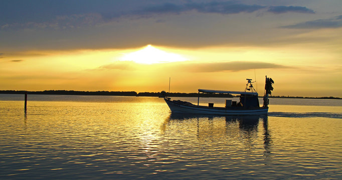 Oranger Sonnenuntergang vor einem See mit einem Fischerboot.