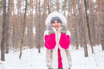 Fototapeta na wymiar Fashion, winter and people concept - Young attractive woman dressed in fur waistcoat over snowy nature background