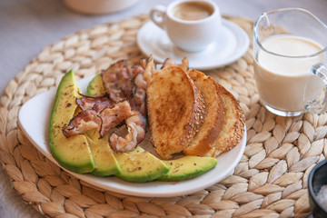 Fried bacon on white plate with cup of coffee and milk jug