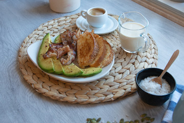 Fried bacon on white plate with cup of coffee and milk jug