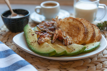 Fried bacon on white plate with cup of coffee and milk jug