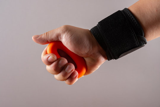 hand with a wrist protective strap doing exercises by squeezing an O ring hand trainer