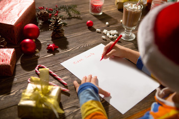 Naklejka na ściany i meble Child writes the letter to Santa Claus on wooden background with decorations.