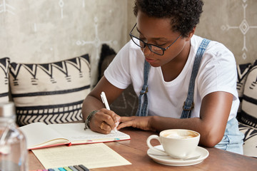 Photo of self employed black professional young entrepreneur writes good ideas to develop her...