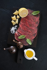 Above view of a black wooden serving board with carpaccio beef, olive oil, parmesan, sea salt, lemon and spices, vertical shot